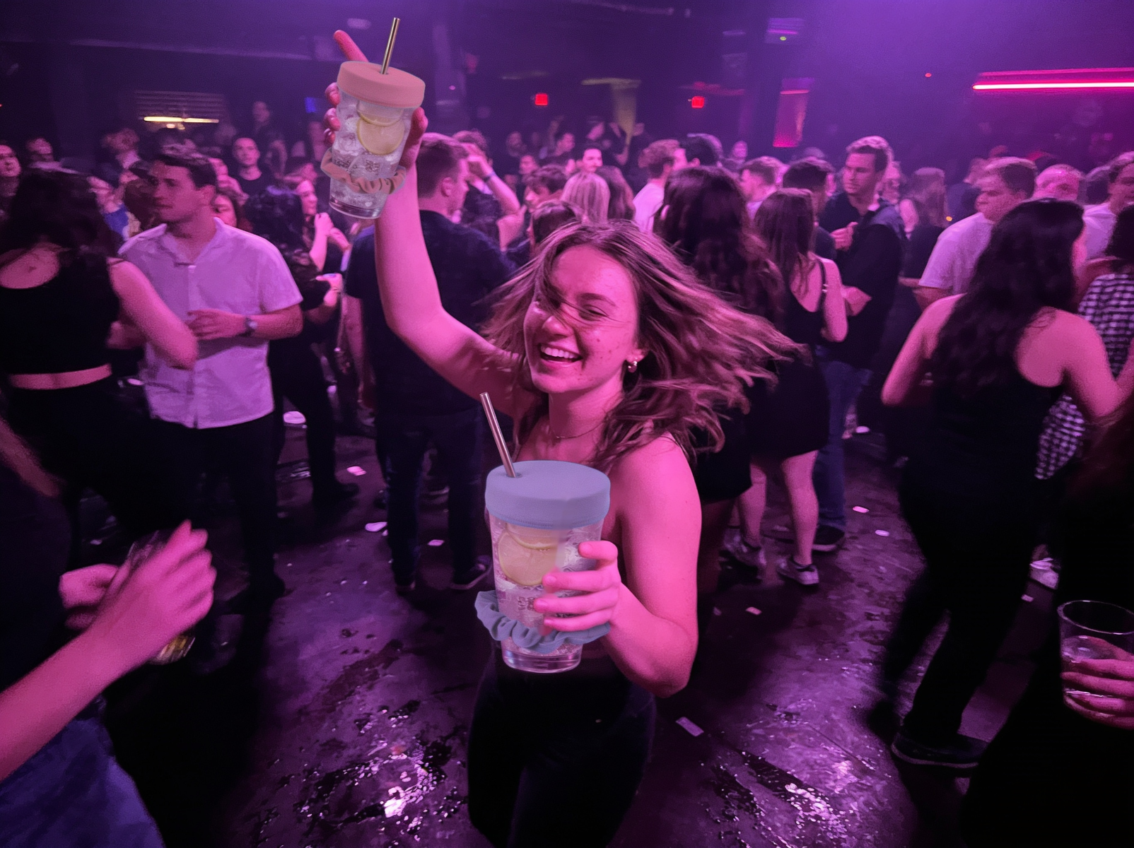 Chica bailando en una discoteca sosteniendo dos vasos con fundas NoSpike